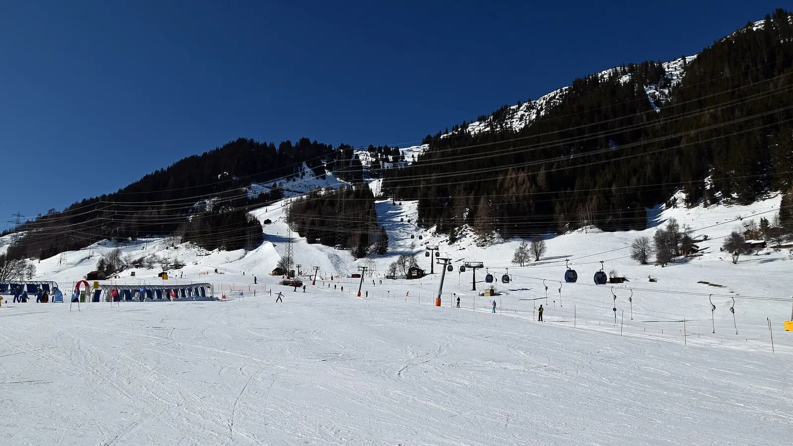 The gentle lower slope at Nasserein in St. Anton am Arlberg, with a children's area on the left, a few skiers and a gondola above.